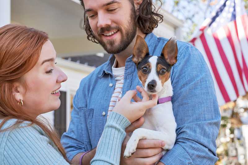 Two people holding terrier dog on front porch of a white house